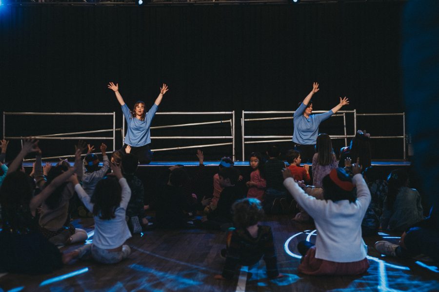 Two people onstage with hands in the air, with audience copying the position