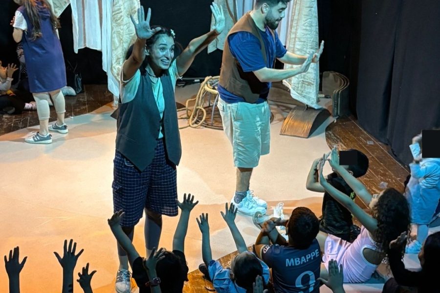 Two performers on the set of Butterflies with an audience of children raising their hands, copying the performers.
