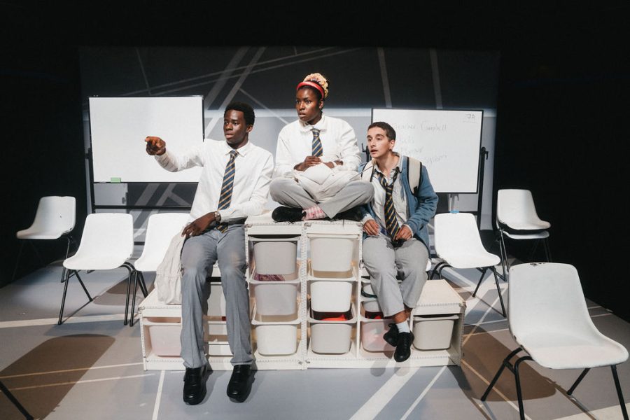 Three of the cast sitting on a white shelving unit looking out, one is pointing and the others are looking where they are pointing.