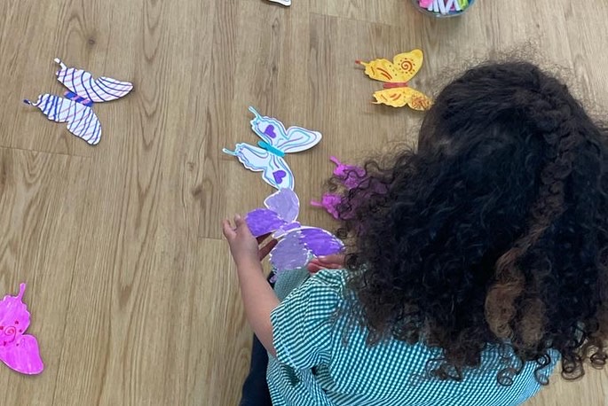 A young persons back of head, sitting on a wooden floor with some coloured in butterflies.