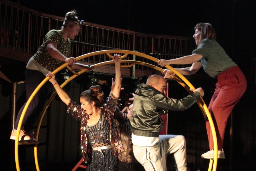 A group of performers climbing on a large german wheel structure