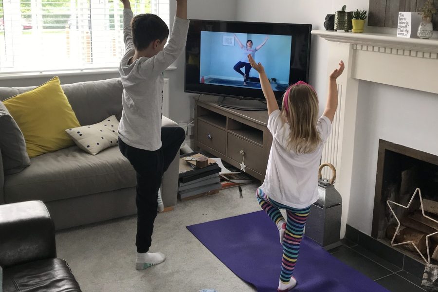 Two young people doing yoga poses whilst watching The Mindfulness Project at Home