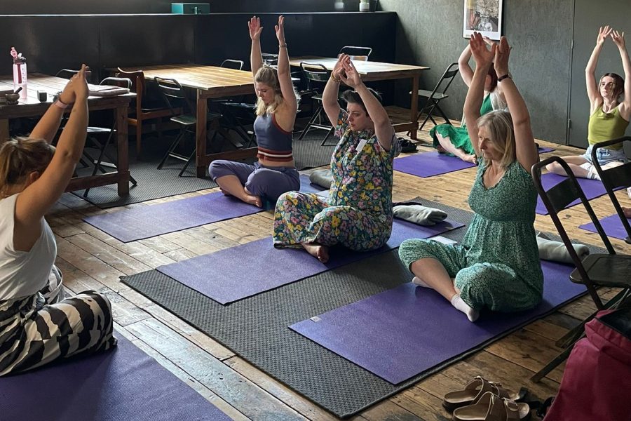A group of IGNITE participants taking part in a Yoga session sitting on Yoga Mats, with arms in the air.