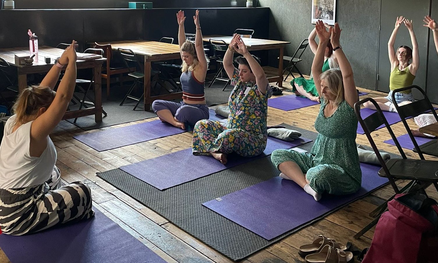 A group of IGNITE participants taking part in a Yoga session sitting on Yoga Mats, with arms in the air.