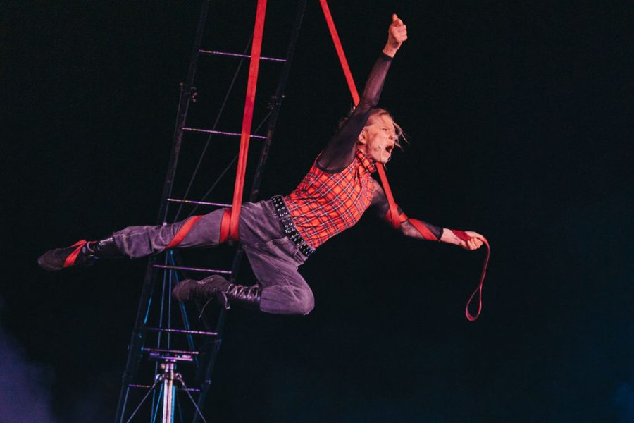 An aerialist in the air, with fist raised in the air and legs outstretched.
