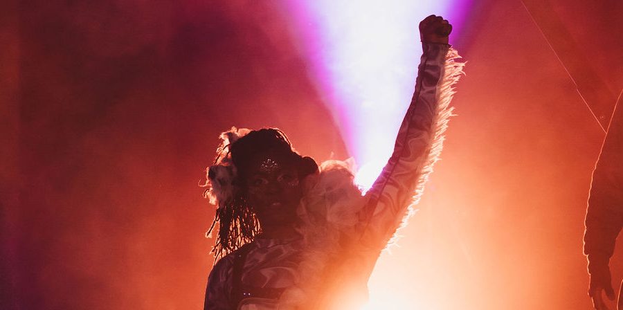 A performer back lit by orange light with their hand in the air.