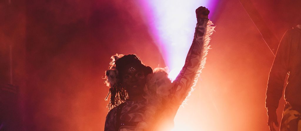 A performer back lit by orange light with their hand in the air.
