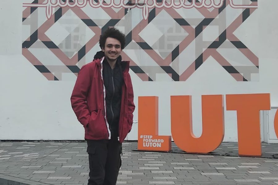 Manuel standing next to a mural in Luton with an orange letter sign saying LUTON.