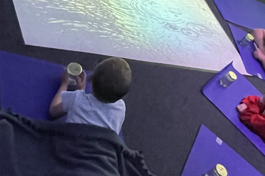 A group of young people on yoga mats circled around a reflective screen on the floor that looks like water.