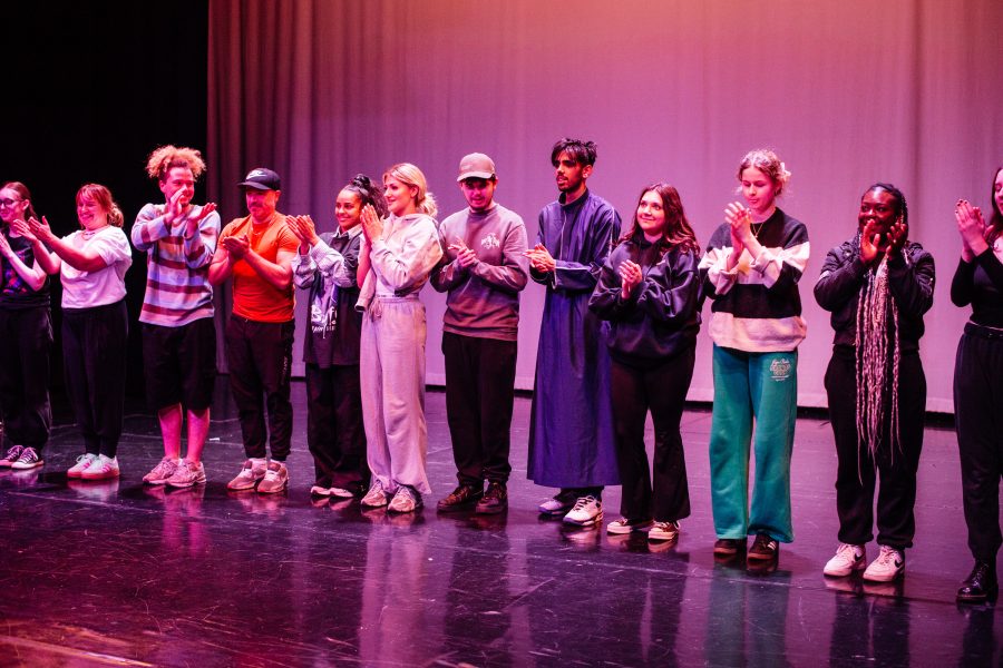 A group of students on stage in a row clapping.