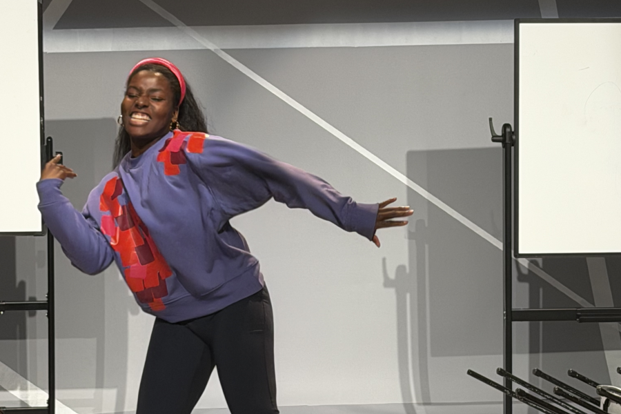 Character Michelle standing up and moving their body in a wiggle warm up smiling looking at the audience.